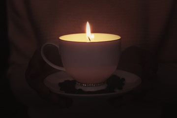 Woman holding cup with burning candle in darkness, closeup