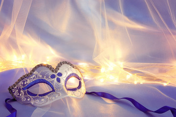 Image of delicate elegant venetian mask over blue silk and tulle fabric background.