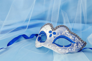 Image of delicate elegant venetian mask over blue silk and tulle fabric background.