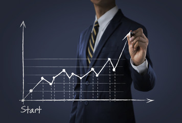 Business growth, progress or success concept. Businessman is drawing a growing graph on dark tone background.