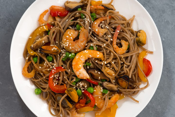 spicy buckwheat noodles with seafood and vegetables on a gray background, closeup