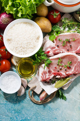 two pieces of pork on a cutting board and fresh foods for cooking soup, vertical top view
