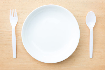 White empty dish, spoon and fork on wooden table background
