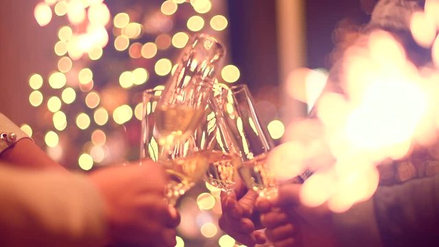 Toasting champagne. Group of people celebrating Christmas party with champagne. Glasses with sparkling wine over glowing background. Slow Motion 4K UHD video footage. 3840X2160