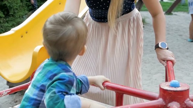Slow motion footage of young mother riding her toddler boy on colorful carousel at park