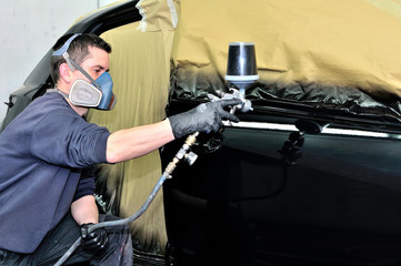 Professional car painter working at a black vehicle.