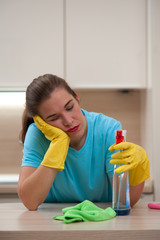 Housewife concept. Portrait of tired beautiful young woman in rubber gloves with spray after cleaning the kitchen