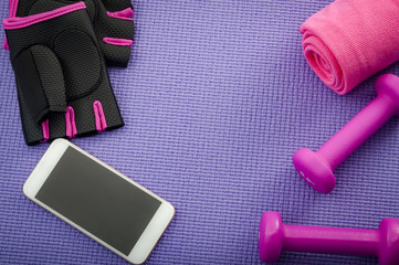 Working out, fitness and bodybuilding, healthy and active lifestyle concept with smartphone, sports towel, pink gloves and gym dumbbells on pink yoga mat floor background with copy space
