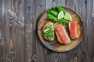 Sandwiches with red fish and avocado, lemon, lettuce, are served on a wooden plate. Top view.