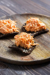 Grated carrots with garlic on rye crackers, served on a wooden plate.