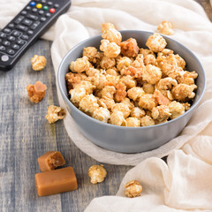 Bowl of a caramel popcorn. Homemade golden sweet corn on wooden grey table. TV remote control