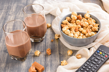 Bowl of a caramel popcorn. Homemade golden sweet corn on wooden grey table. TV remote control and cocoa drinks