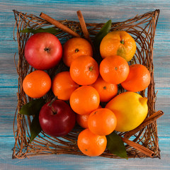 Fresh mandarin orange with green leaves, lemon and apple in the basket on wooden background