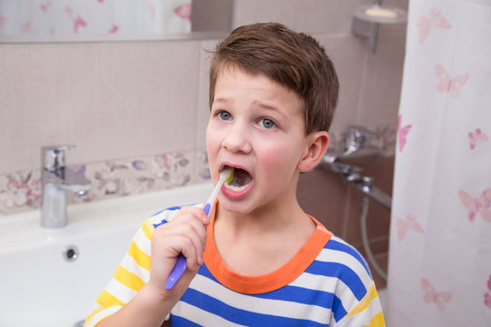 Sad little boy cleaning his teeth in the bathroom