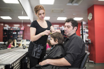 Hairdresser cuts little baby hair with fathers help