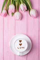 Fototapeta na wymiar Happy Valentine's Day. Coffee cappuccino, two hearts, inscription LOVE and pink tulips on a pink background. Top view, free space