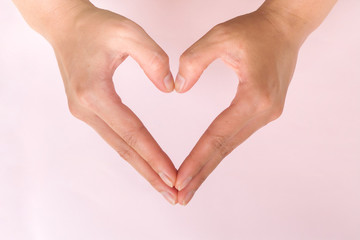 Obraz premium Woman hands make heart shape on pink background. Symbolic of love. Valentine theme.