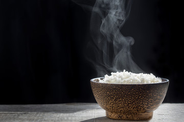 Cooked rice with steam in wooden bowl on dark background,hot cooked rice in bowl selective...