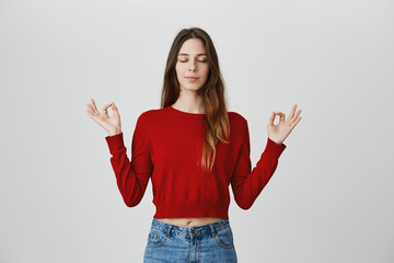 Meditating. Healthy lifestyle, positive emotions. Portrait of good-looking young european girl with long hair in red sweater and denim jeans posing for photo with closed eyes an relaxed expression