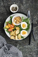 Fresh spring salad with boiled egg, arugula, salad, tomatoes, pecans and crispy toasted bread croutons in a large dish on a gray background. Top view..