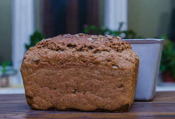 Fresh loaf of homemade black bread with bread form on wooden surface