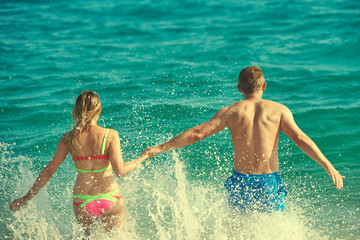 Caucasian couple running into the sea water. Back view.
