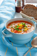 Soup of chicken and vegetables with mushrooms and tomatoes in a blue tureen with handles on a table with blue cloth.
