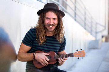 Friendly hipster man with warm personality smiling and playing a ukulele guitar