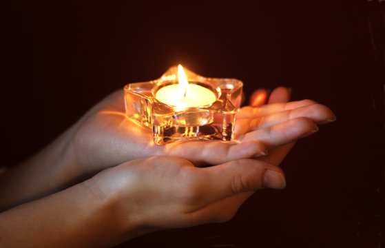 hands of a woman holding a lit tea light in star shape