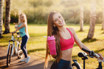 Fitness bicycle. Team of girls bike with bottle of water in park on sunset background