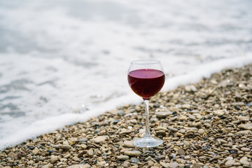 A glass of red wine on the pebble beach at the sea coast. Vacation pleasure concept