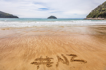 Word NZ hashtag written in sand on New Zealand beach for social media following online advertisement concept. Abel Tasman National Park beach, South Island, New Zealand.