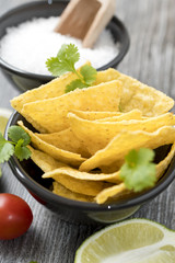 Corn tortilla chips in black bowl on rustic wooden table. 