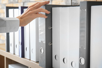 Young woman taking folder with documents from shelf in archive