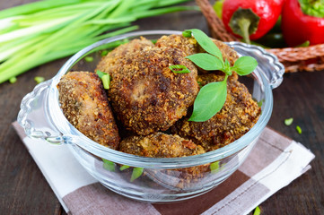 Small meat cutlets in a glass bowl on a dark wooden background.