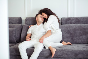 Obraz premium Portrait of young couple sitting together on grey sofa in modern white apartment or domestic room