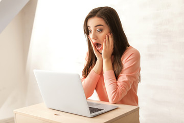 Emotional young woman with laptop at home