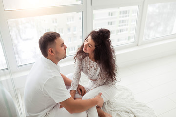 Fototapeta premium Happy couple or marriage in their new home sitting near the window and hugging together