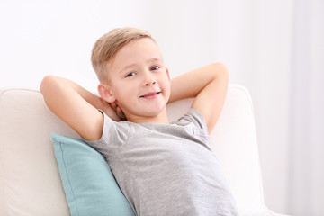 Cute boy resting in armchair with soft pillow at home