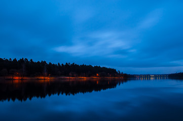 Park with lights near the river in the night. City lights in the distance.