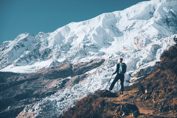 Standing young woman with backpack on the mountain peak and looking on beautiful mountains and glacier at sunset. Landscape with girl, rocks with snowy peaks,blue sky in Nepal.Hiking, travel. Vintage