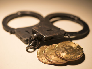 Golden bitcoins and handcuffs on wooden table