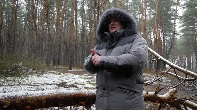 4k middle aged man with warm jacket freezes in winter pine wood wide shot
