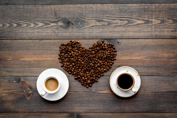 Cups of freshly brewed full-bodied and milky coffee near beans in heart shape on dark wooden table top view copyspace. Coffee background.
