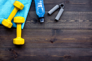 Fitness equipment. Dumbbells, expander, water on dark wooden background top view copyspace