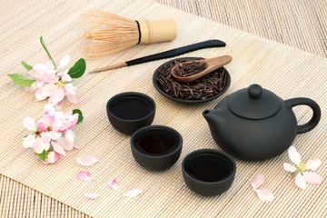 Obraz na płótnie Canvas Kuchika Japanese roasted green twig tea with teapot and cups, stirrer, whisk and blossom flowers on bamboo background. Has many health benefits including rejuvenating properties.