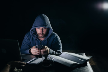 mysterious criminal man in the hood hacks the password on the smartphone, in the dark