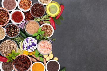 Fresh and dried herb and spice selection with edible flowers and olive oil forming an abstract border on slate background.