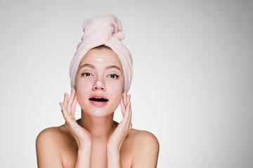 young attractive girl with pink towel on her head applying moisturizer on face