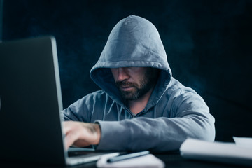 mysterious bearded man hides his face under the hood, hacks the laptop, does something illegal and dangerous